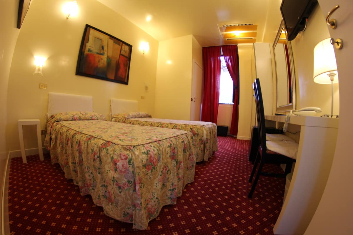 A hotel room with two beds, a sitting area with a chair and a table, a bathroom with a mirror and a sink, and a painting on the wall.