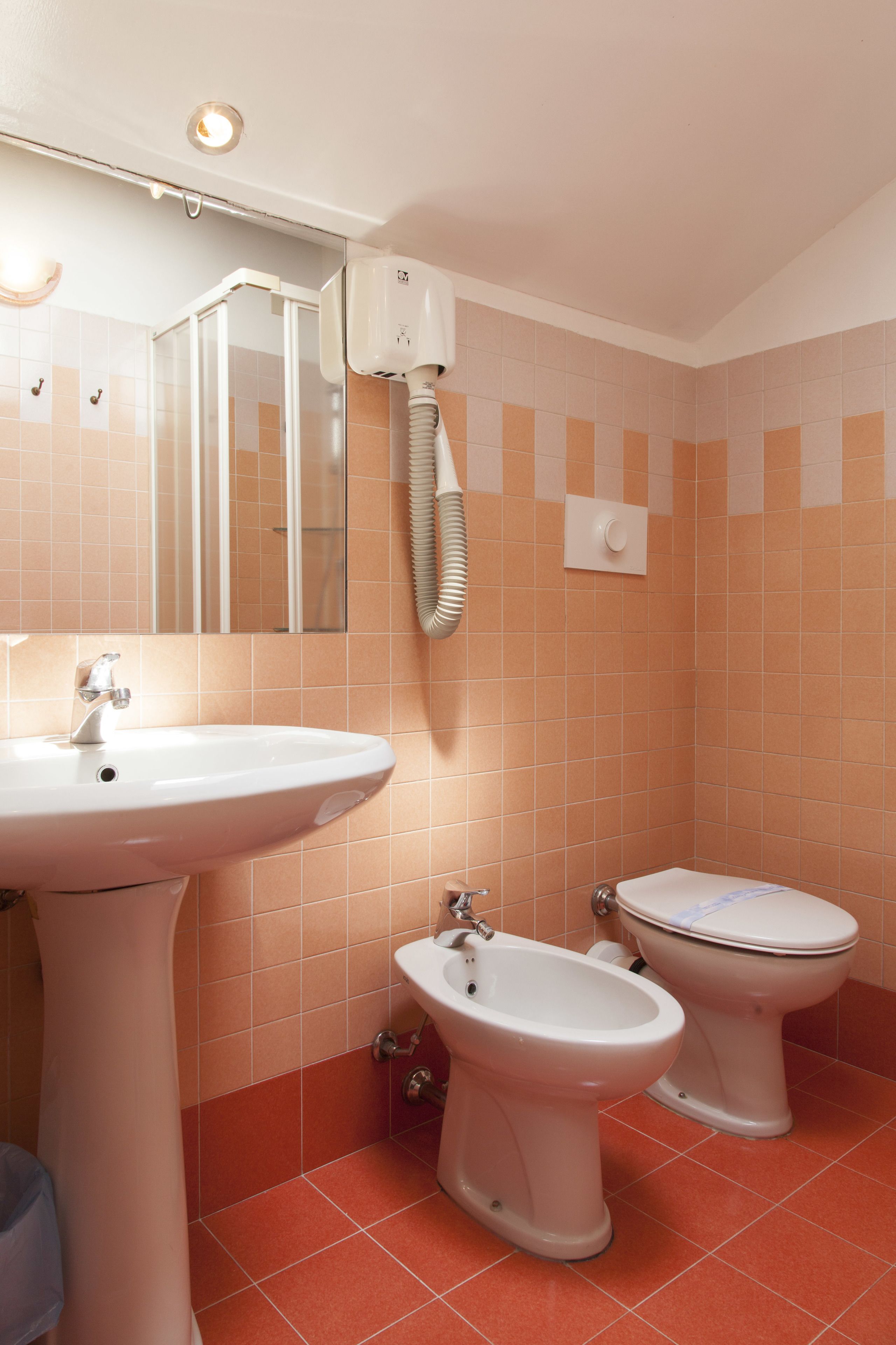 A bathroom with a sink, bidet, toilet, and a hairdryer mounted on the wall.