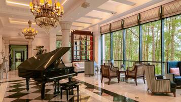 A grand lobby with a piano, seating area, large windows, and a decorative bookshelf.