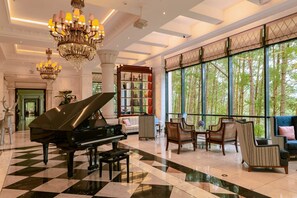 A grand lobby with a piano, seating area, large windows, and a decorative bookshelf. - Dalat Edensee Lake Resort & Spa (Xuan Huong - Da Lat)