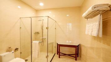 A bathroom with a glass-enclosed shower, a toilet, a vanity with a marble countertop, and a towel rack with folded towels.