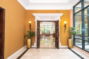 A Banquet Restaurant with a grand entrance, large potted plants, and a spacious interior with tables and chairs.