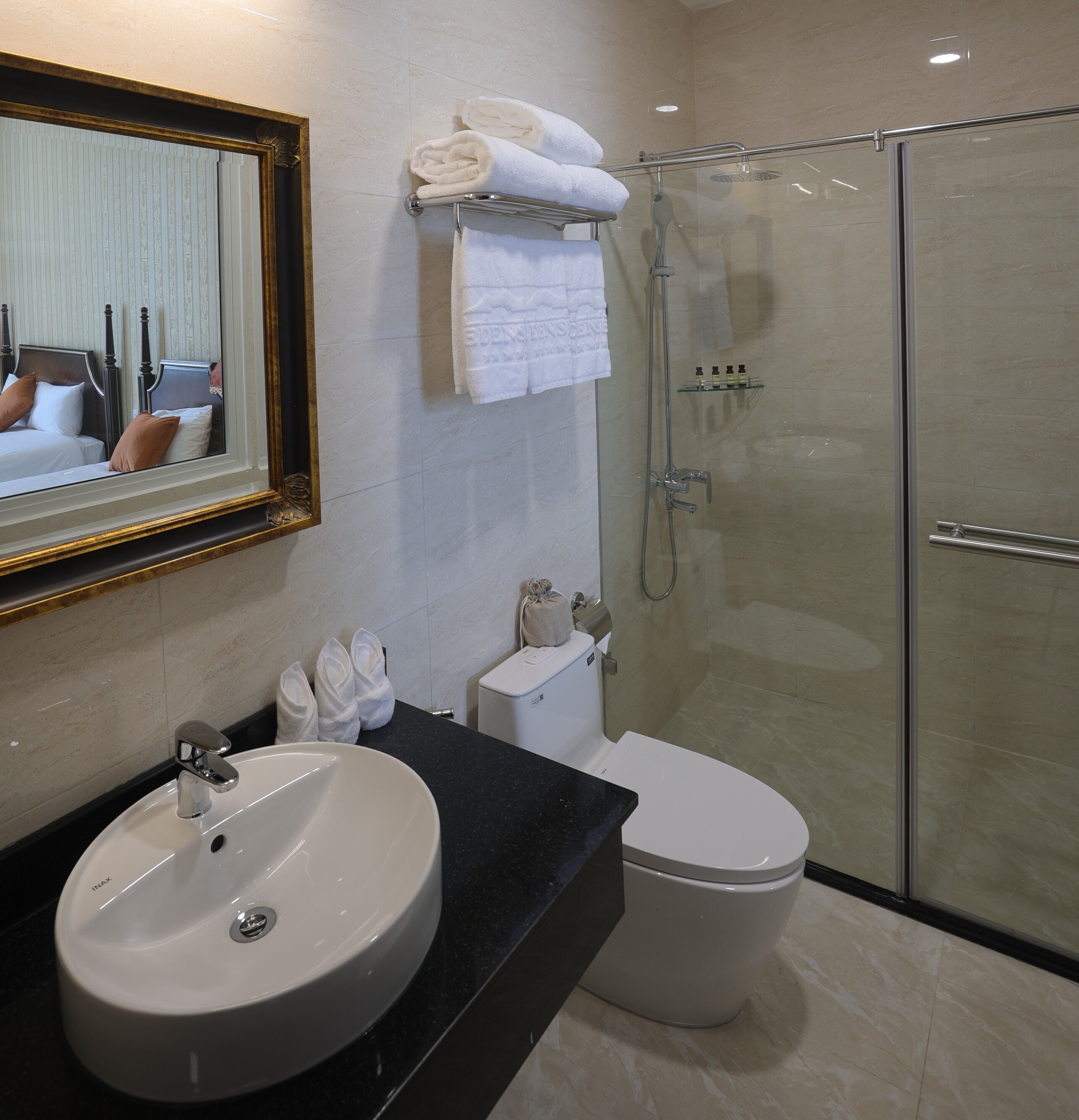 A bathroom with a round sink, a toilet, a glass shower enclosure, and a mirror with a gold frame.
