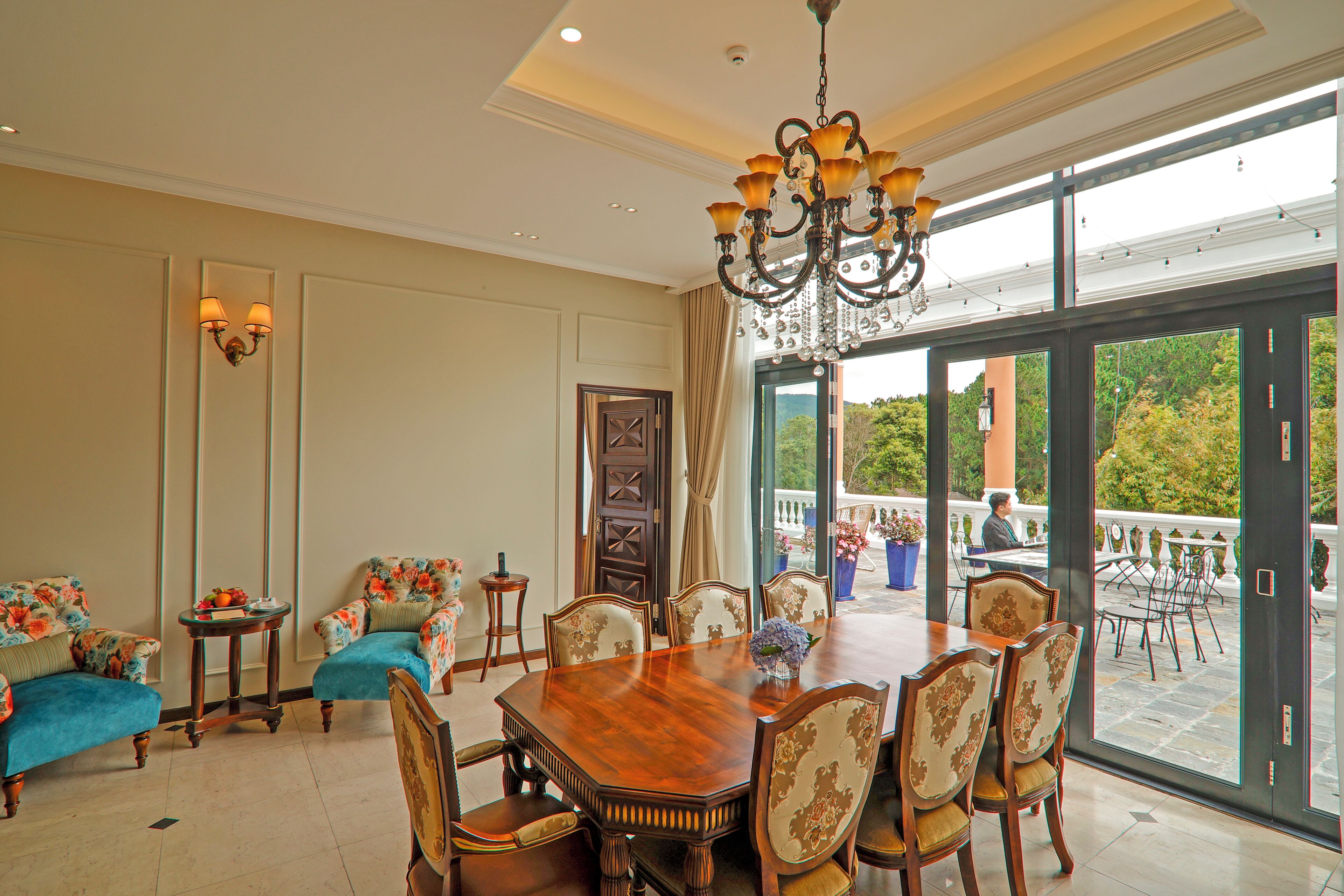 A dining area with a large wooden table, floral upholstered chairs, and a chandelier.