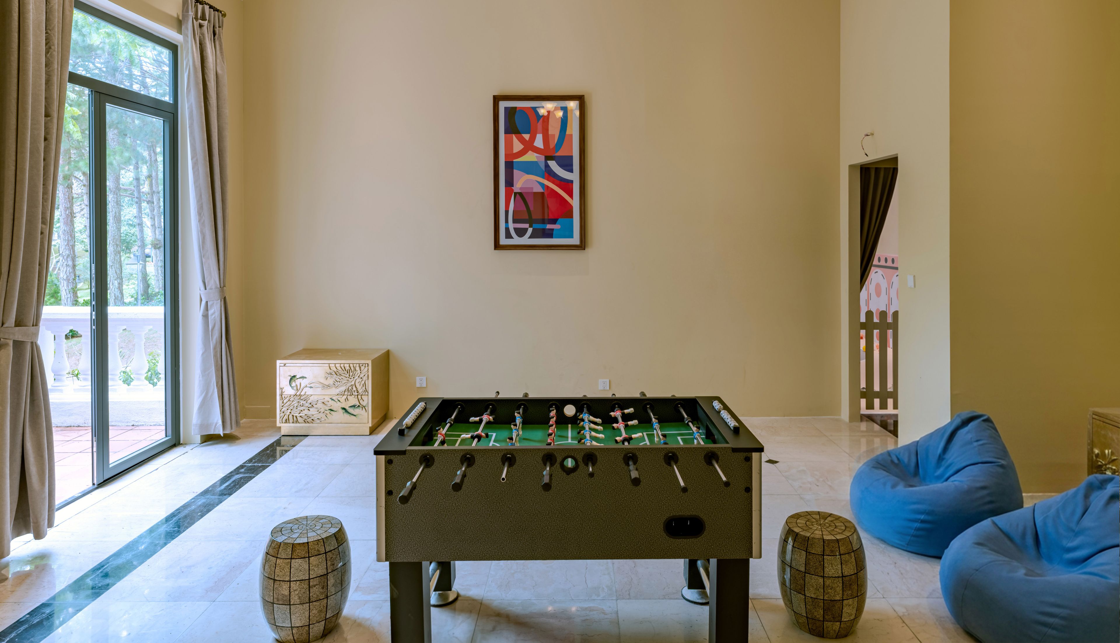 A room with a foosball table, a painting, and a view through a window.