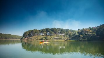 Um lago tranquilo com um caiaque e duas pessoas remando. Casas são visíveis na margem.