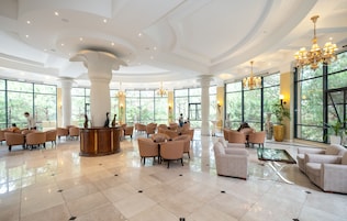 A spacious lobby with a reception desk, comfortable seating, large windows, and elegant chandeliers.