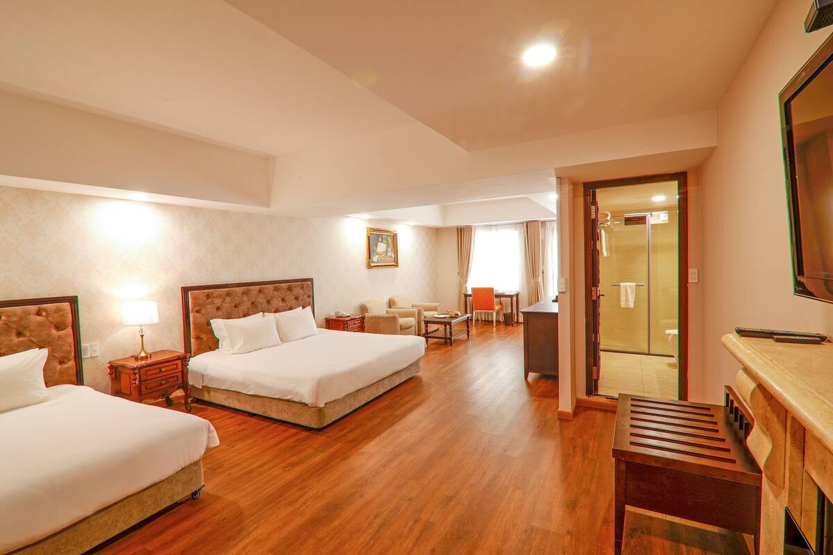 A hotel room with two beds, a desk, a chair, a small table, and a TV.