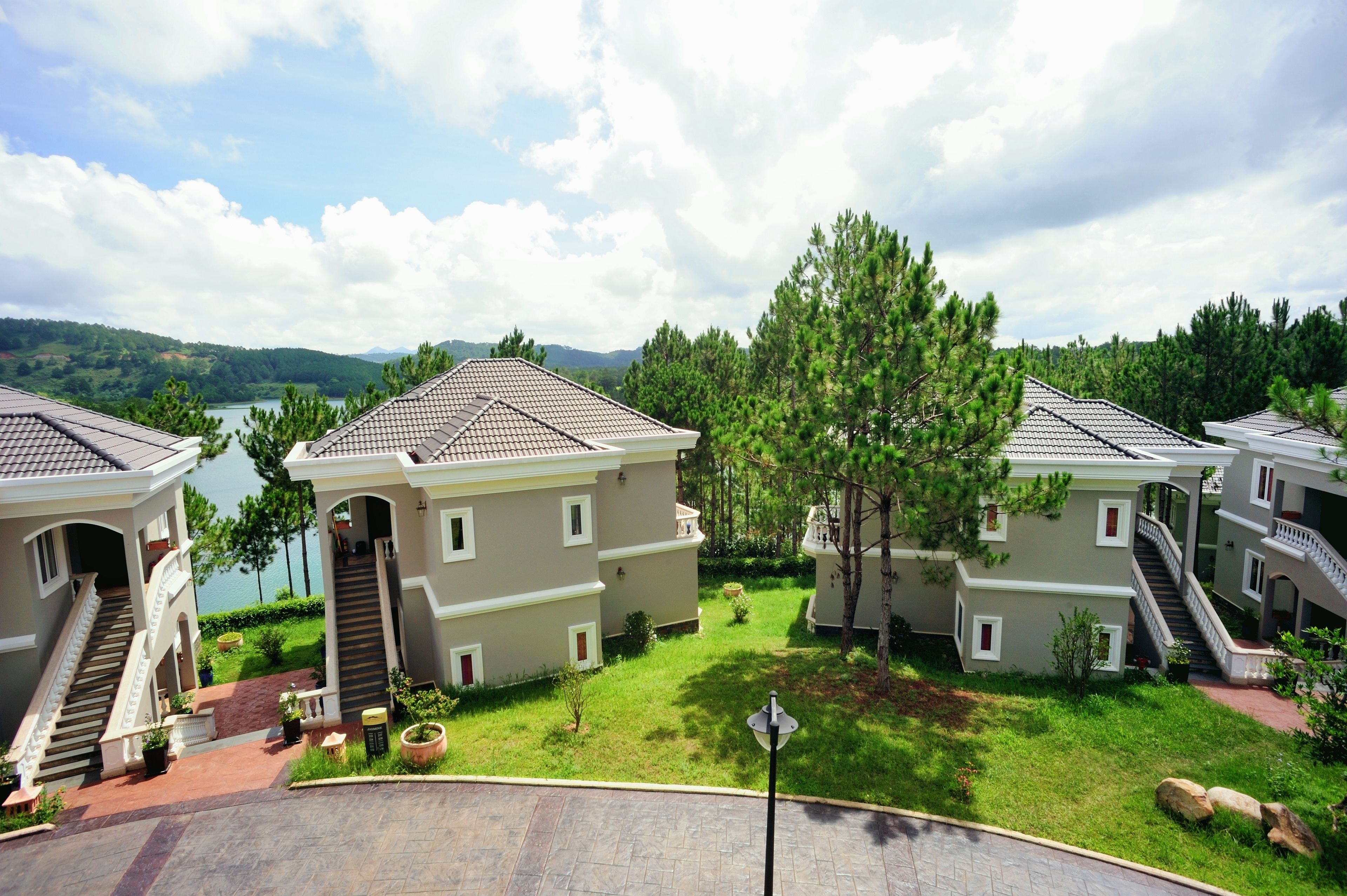 A residential area with multiple houses, each with a staircase leading to the entrance. There is a well-maintained lawn and a body of water in the background.