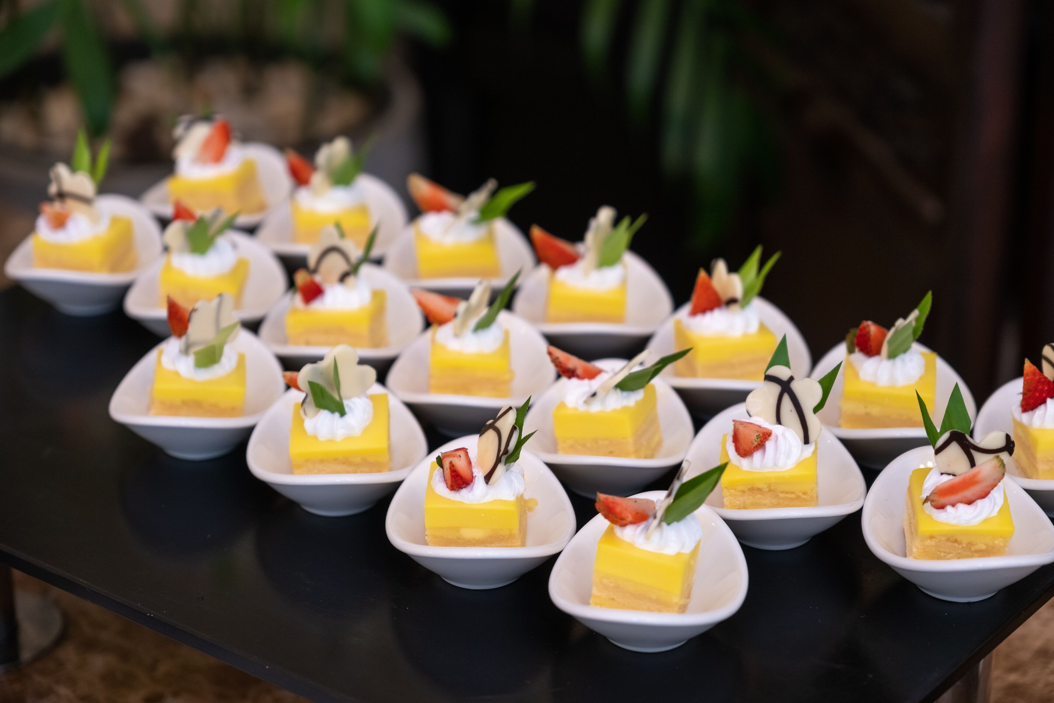 Una mesa con varios pequeños postres, cada uno cubierto de crema batida y decorado con fresas y hojas.