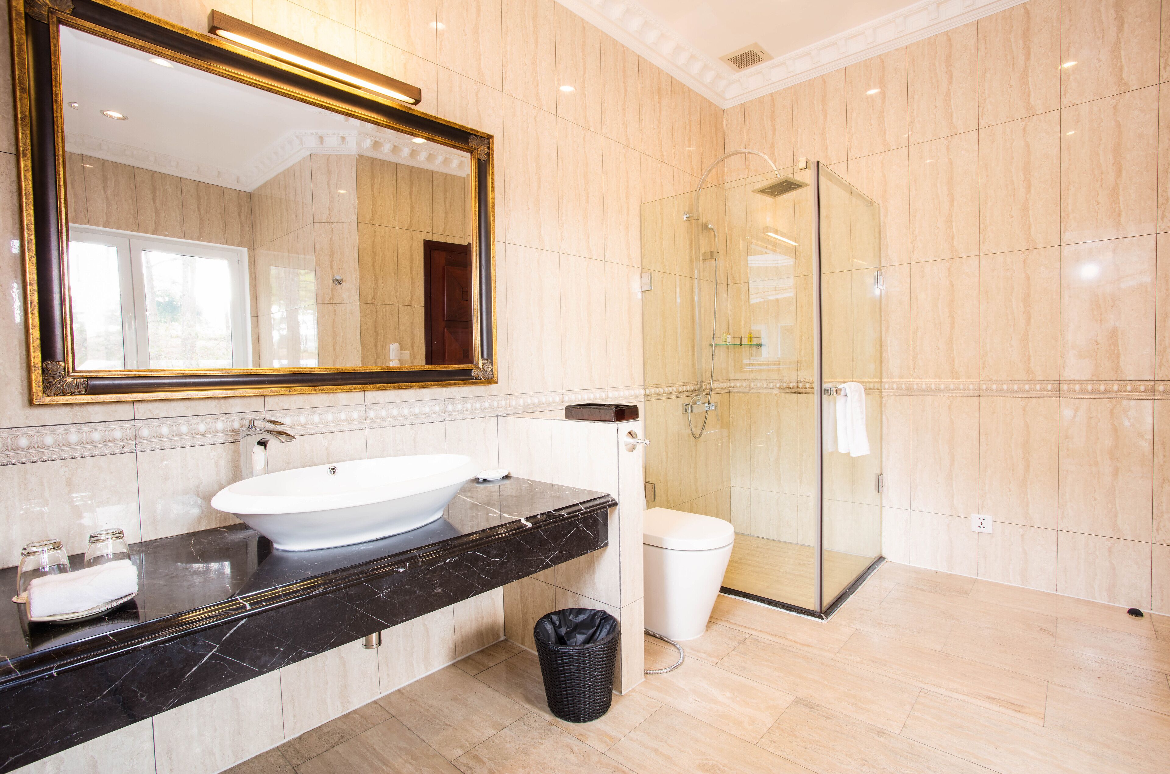 Un baño moderno con un espejo grande, un lavabo blanco, ducha con mampara de cristal y suelo de mármol.