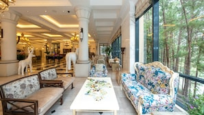 A spacious lobby with high ceilings, large windows, and a view of a forest. There are several sofas and chairs arranged for seating. - Dalat Edensee Lake Resort & Spa (Xuan Huong - Da Lat)
