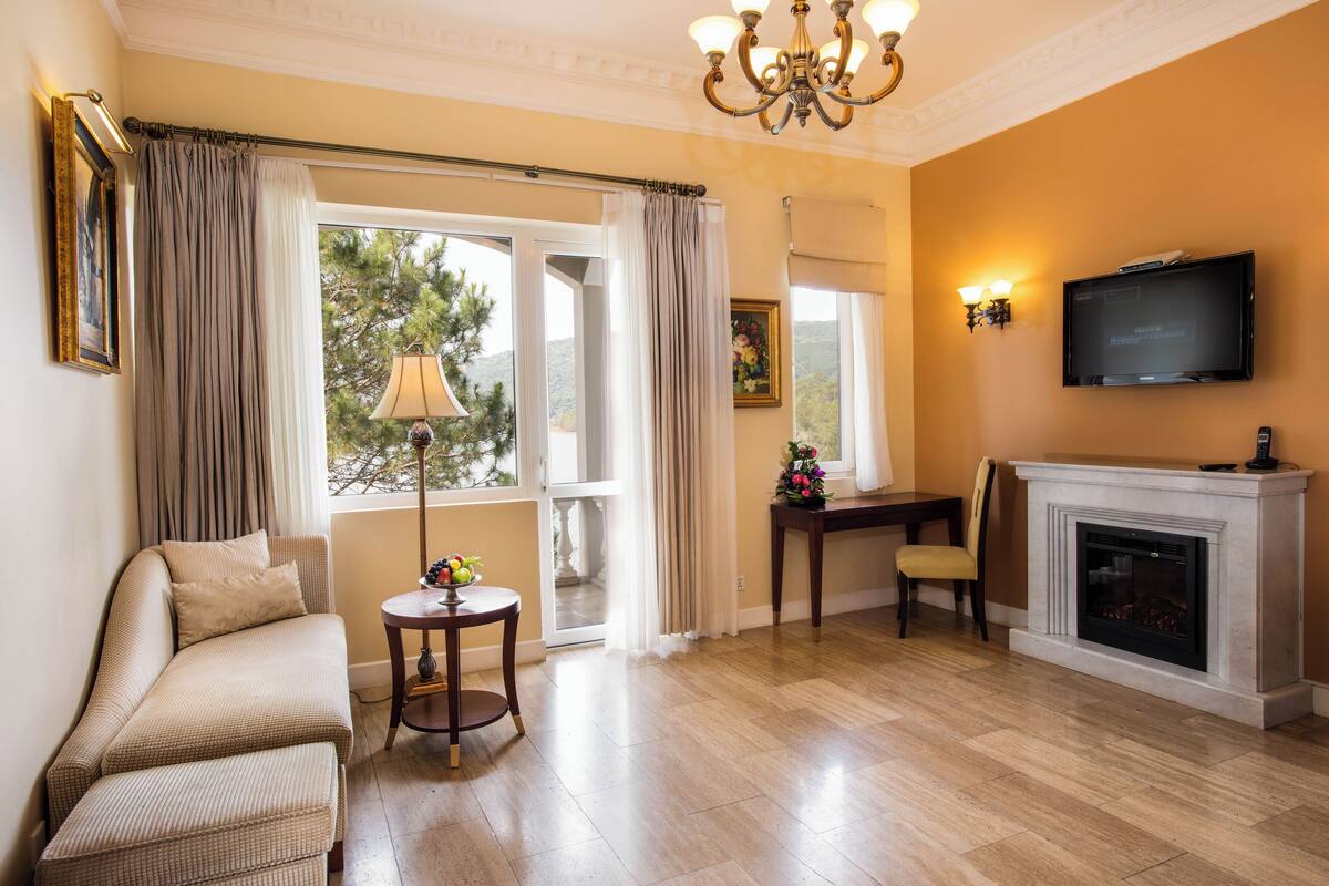 A living room with a sofa, a small table with a lamp, a fireplace, and a television mounted on the wall.