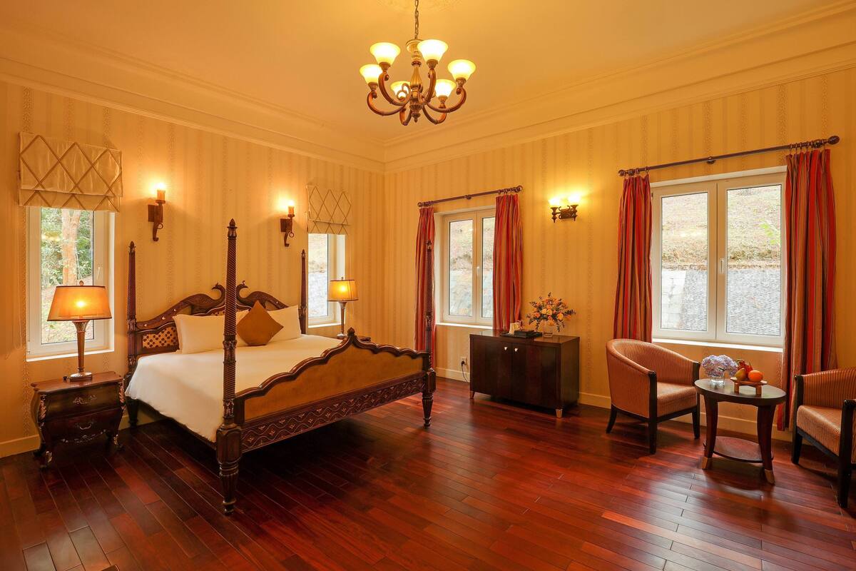 A spacious bedroom with a four-poster bed, a chandelier, and two chairs.