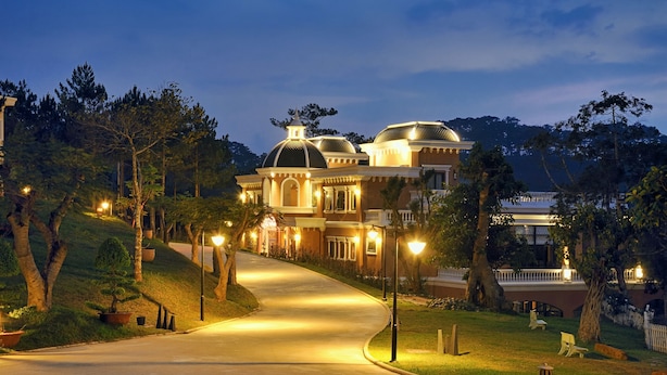 A large, two-story mansion with a curved driveway, surrounded by trees and well-lit by street lamps. - Dalat Edensee Lake Resort & Spa (Xuan Huong - Da Lat)