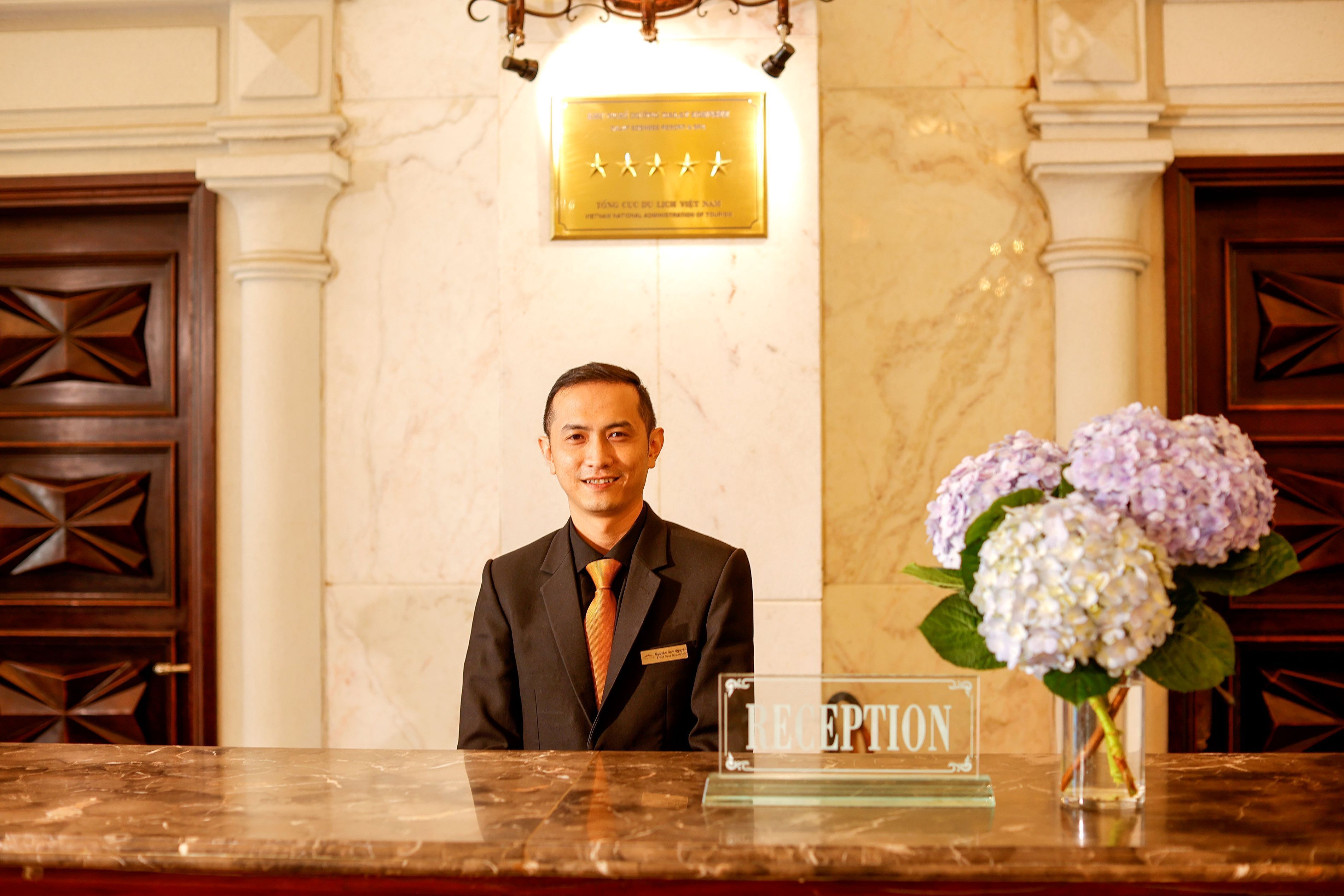 A reception desk with a plaque above it, a nameplate, and a vase with flowers.