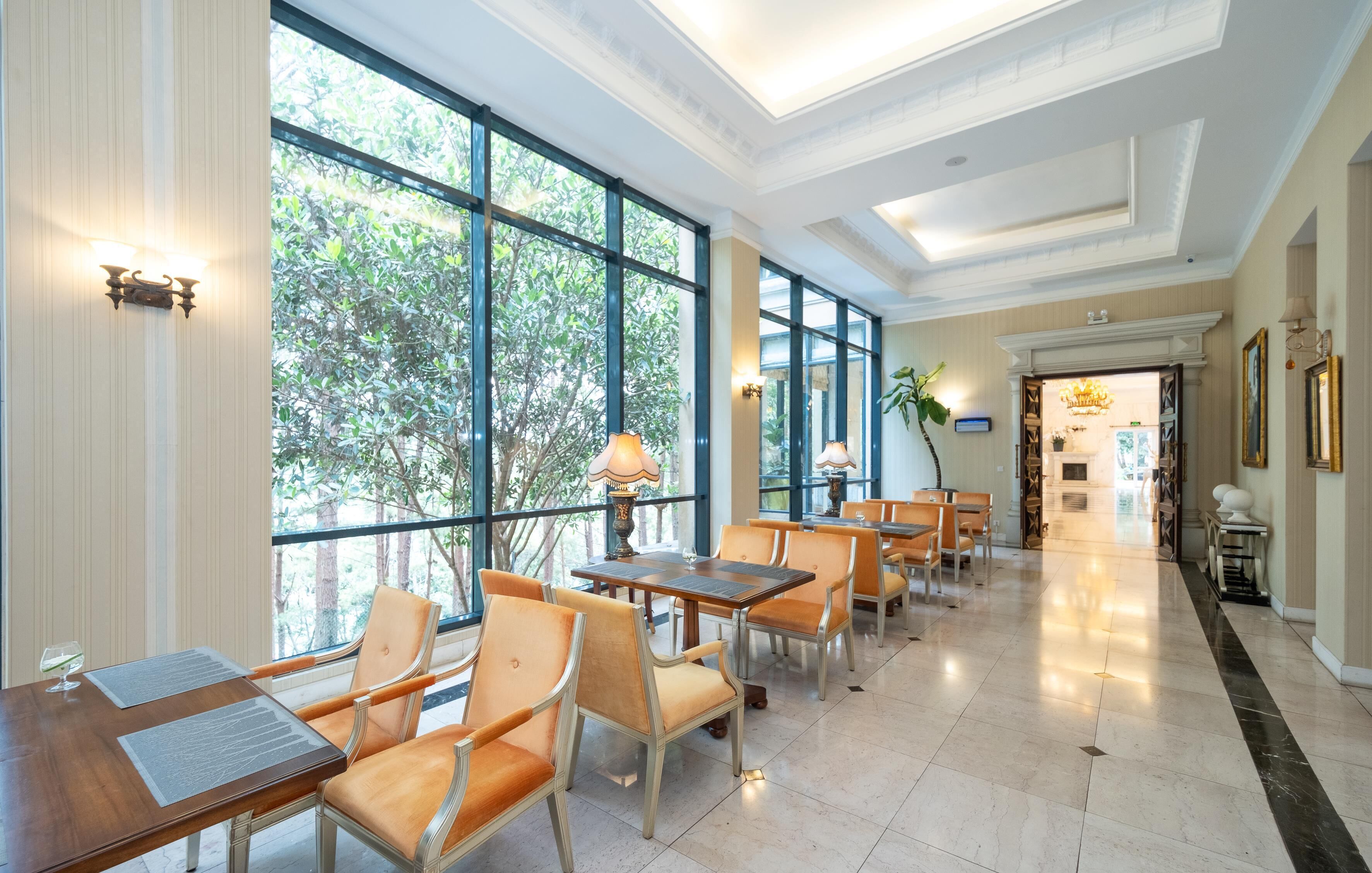 A spacious hotel lobby with large windows, comfortable seating, and a chandelier.