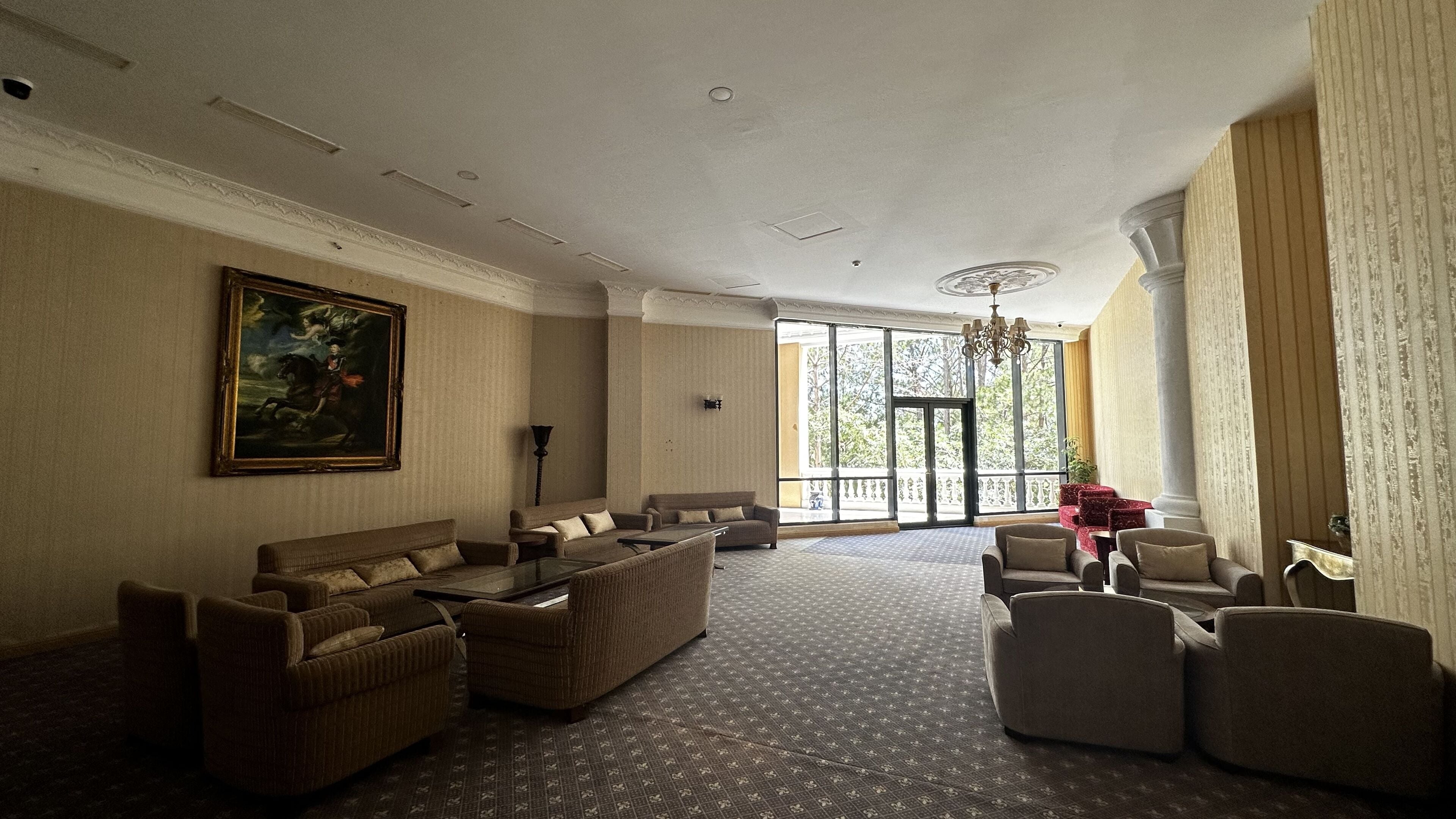 A spacious living room with a large window, a chandelier, and a painting on the wall.