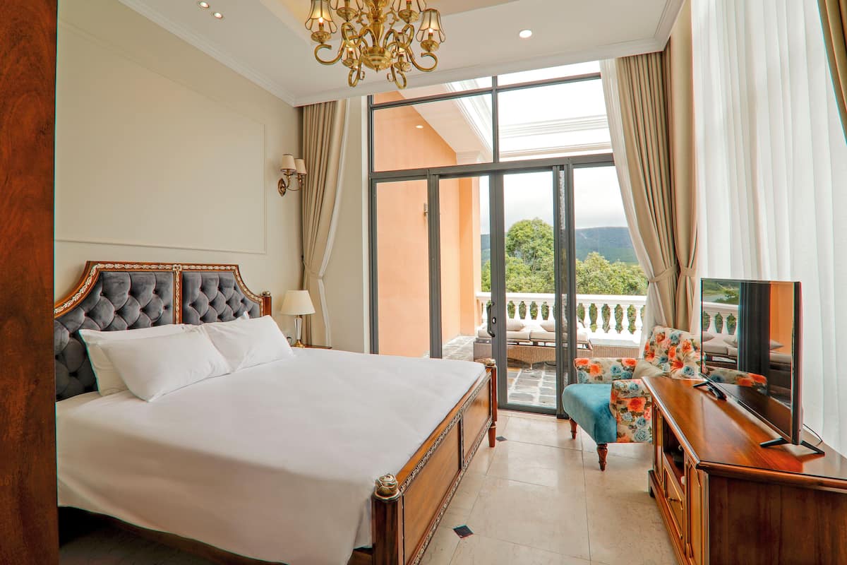A spacious bedroom with a large bed, a TV, and a balcony with a view.