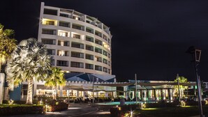 A multi-story hotel with a pool area, outdoor seating, and palm trees.