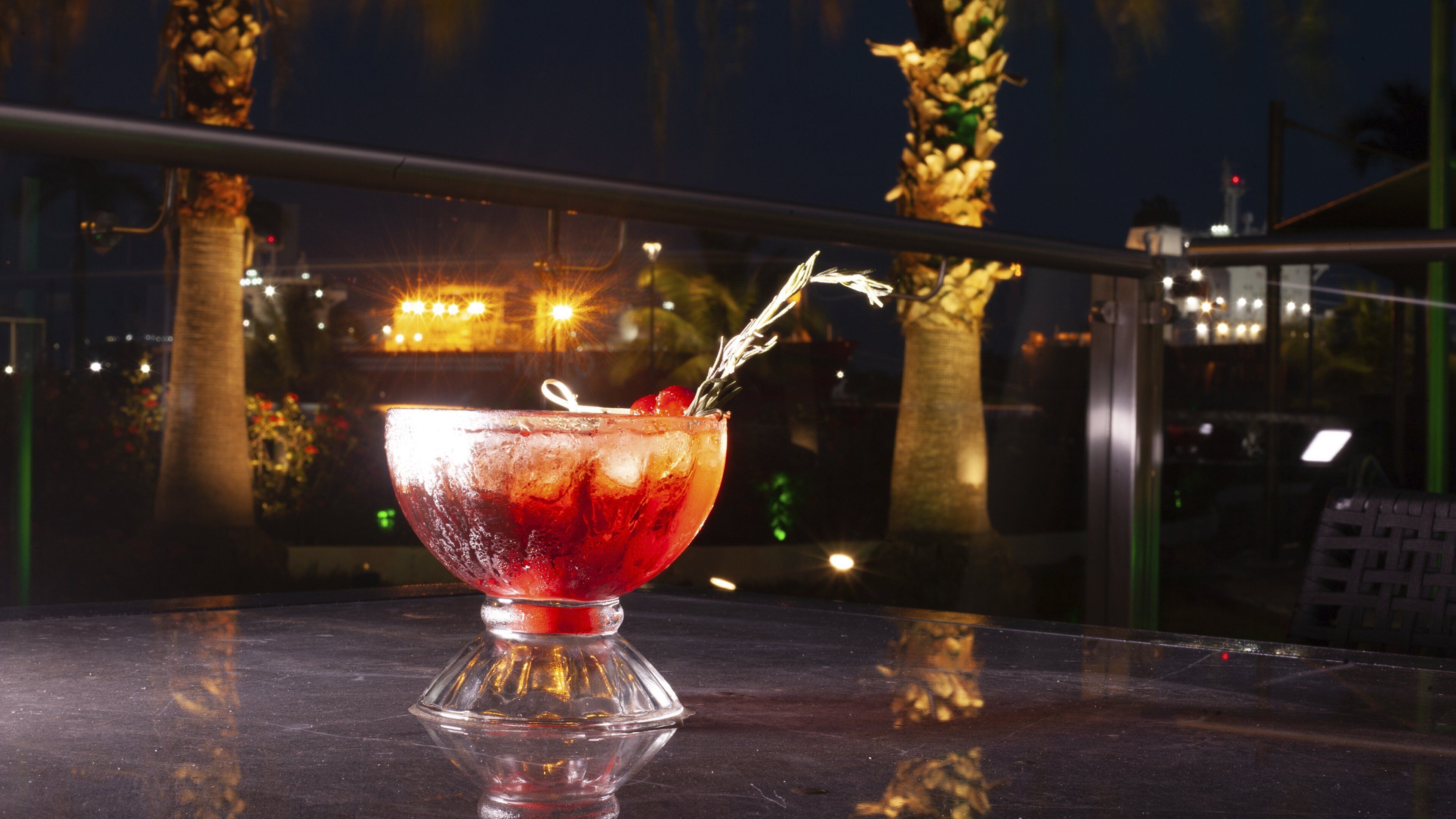 A cocktail glass on a reflective surface with a cityscape in the background.