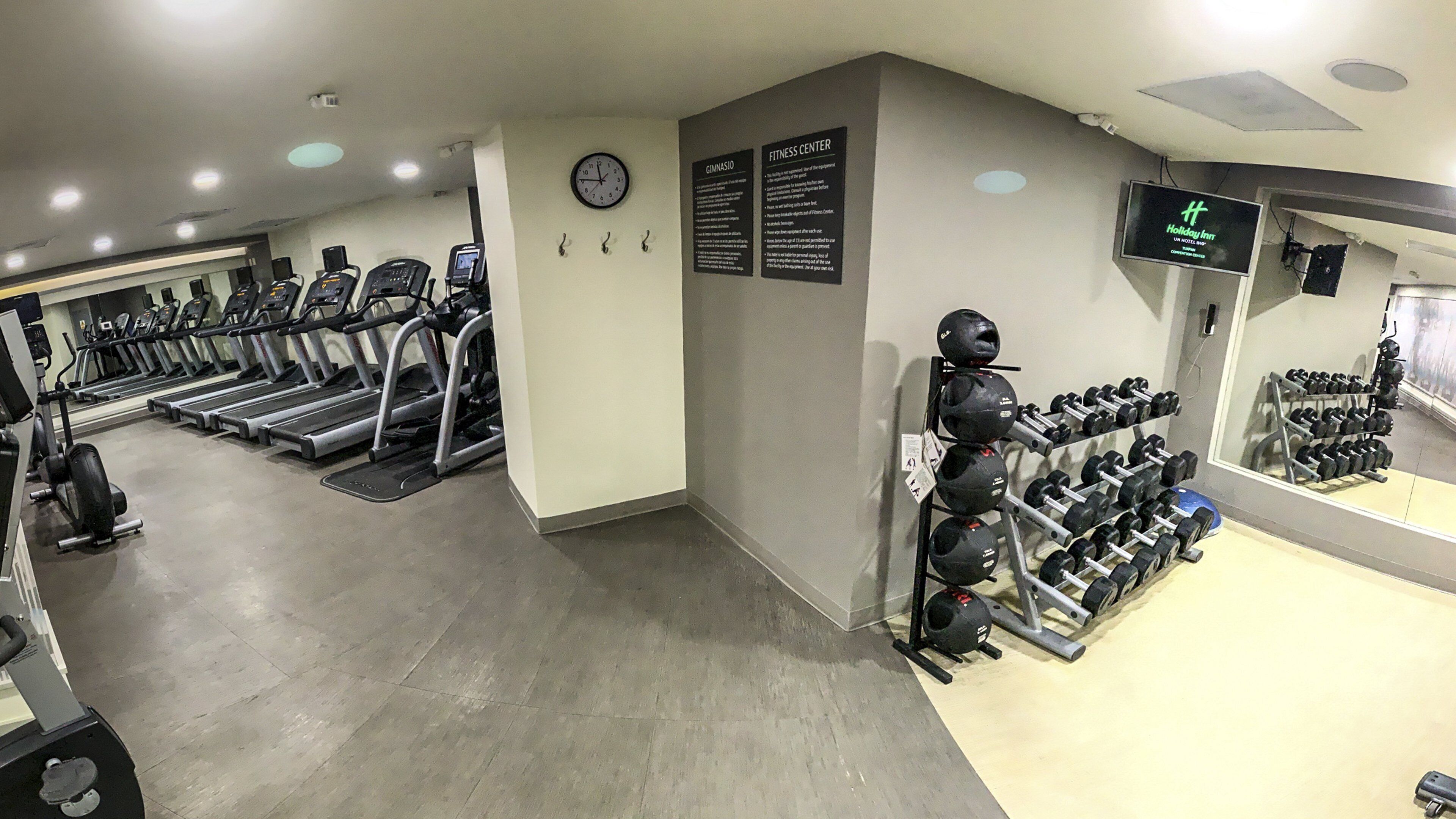 Un gimnasio con cintas de correr, mancuernas y un reloj en la pared.