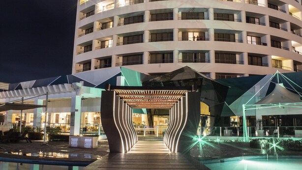 A modern hotel with a circular building, a pool area, and a covered walkway.