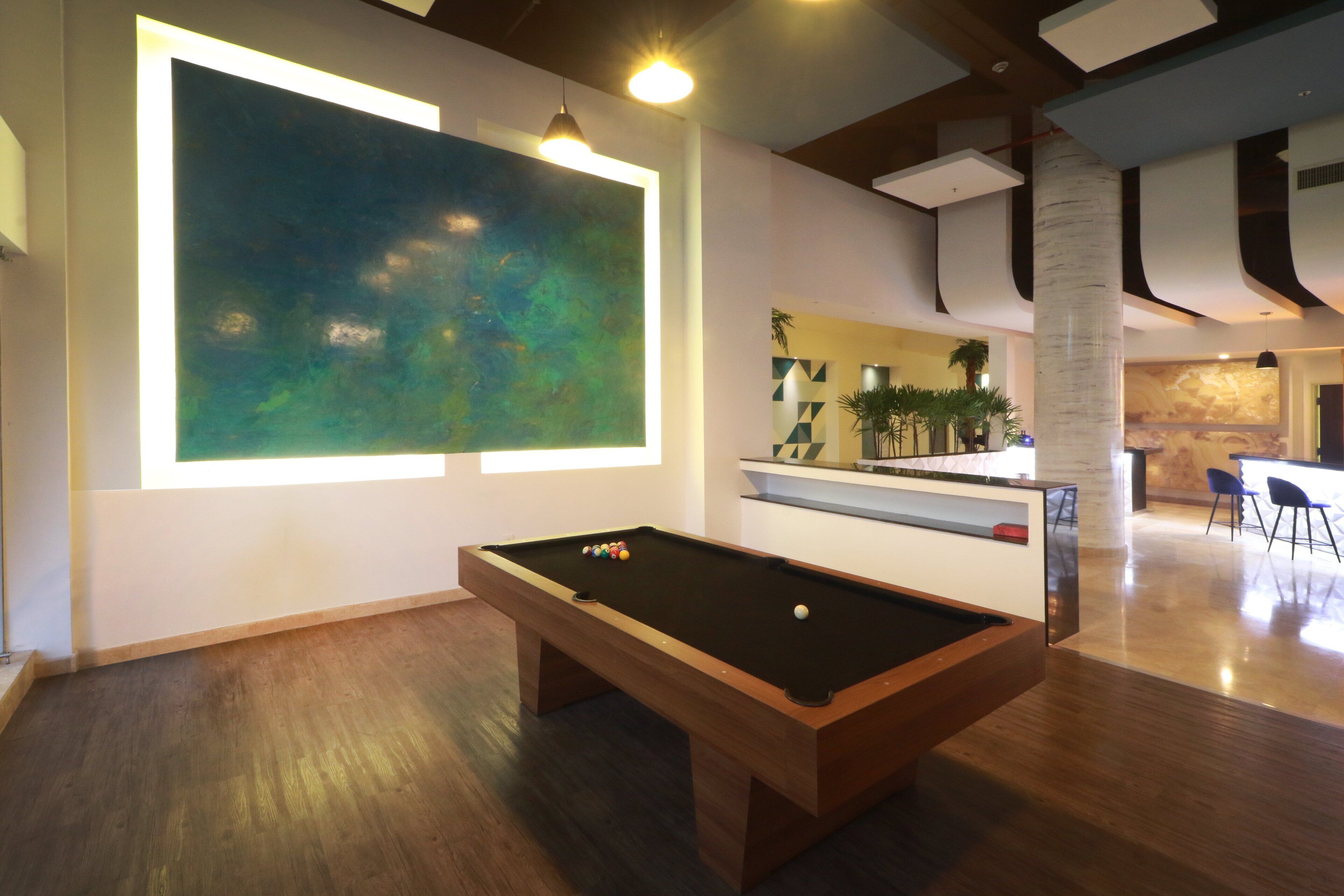 A pool table in a modern room with a large abstract painting and a bar area in the background.