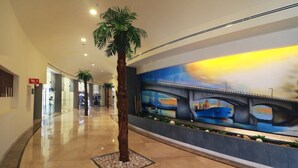 A spacious corridor with a polished marble floor, a palm tree, and a mural depicting a bridge.