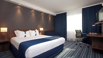 A hotel room with a large bed, a desk, a chair, and a television.
