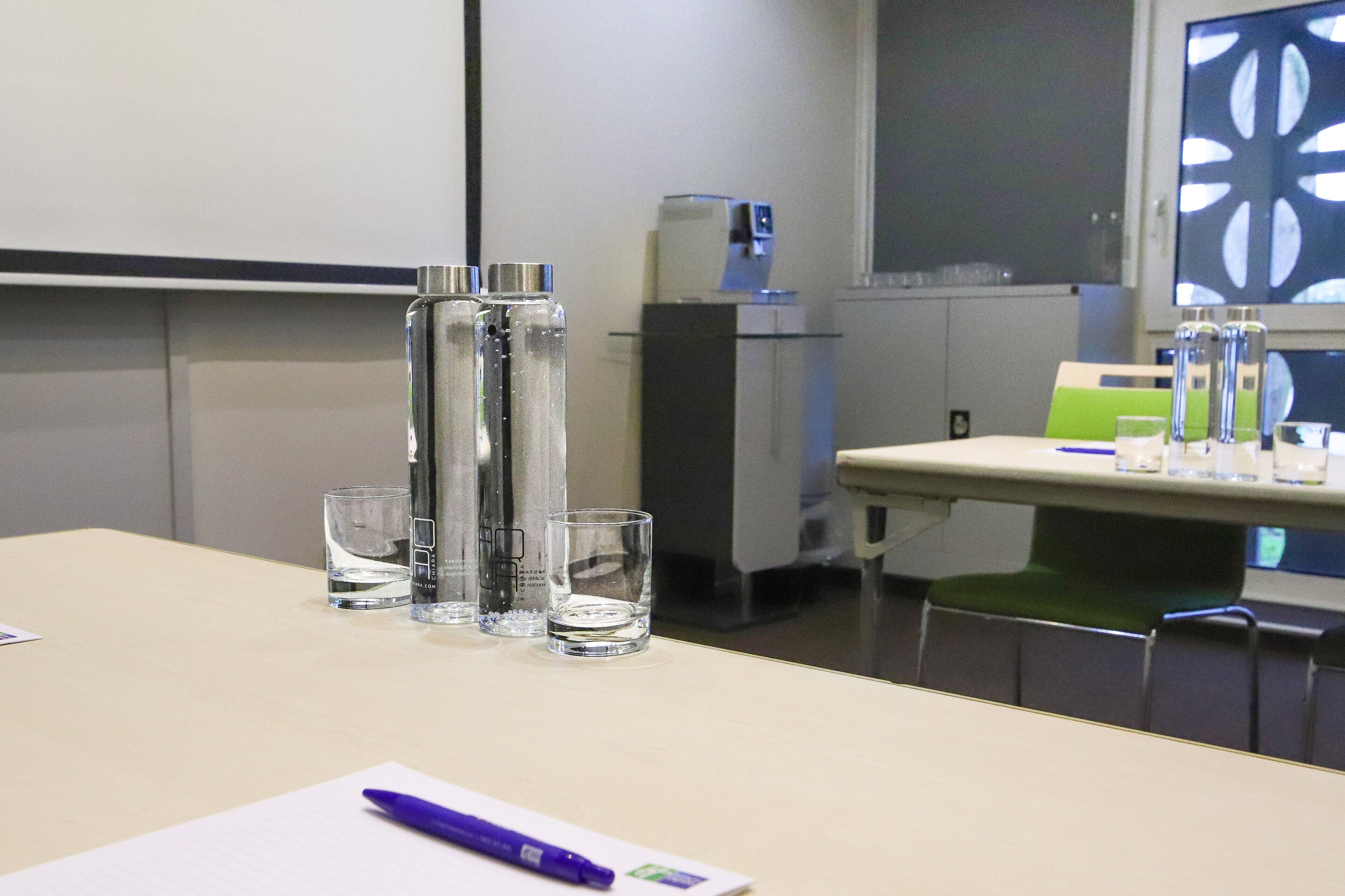 A conference room with a table, chairs, a projector screen, and a water dispenser.