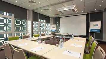 A conference room with a large screen, tables with chairs, water bottles, and a 'Welcome' sign.