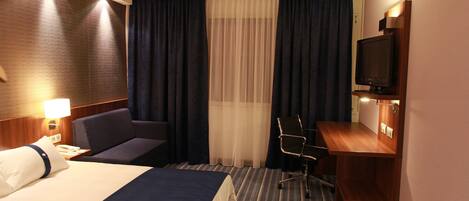 A hotel room with a bed, a desk, a chair, a television, and a window with curtains.