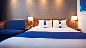A hotel room with a large bed, two bedside lamps, a wooden headboard, and a blue accent wall. - Holiday Inn Express Strasbourg - Sud by IHG (Geispolsheim)