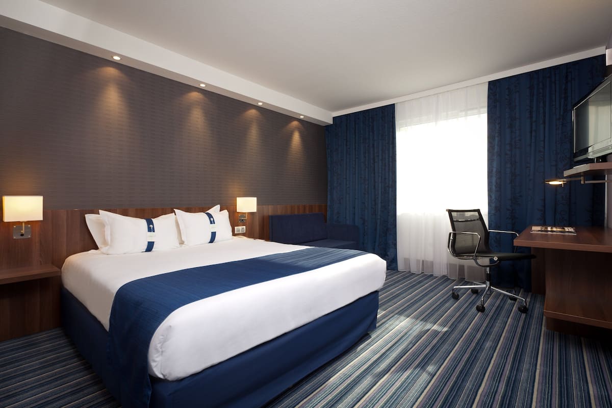 A hotel room with a large bed, a desk, and a chair.