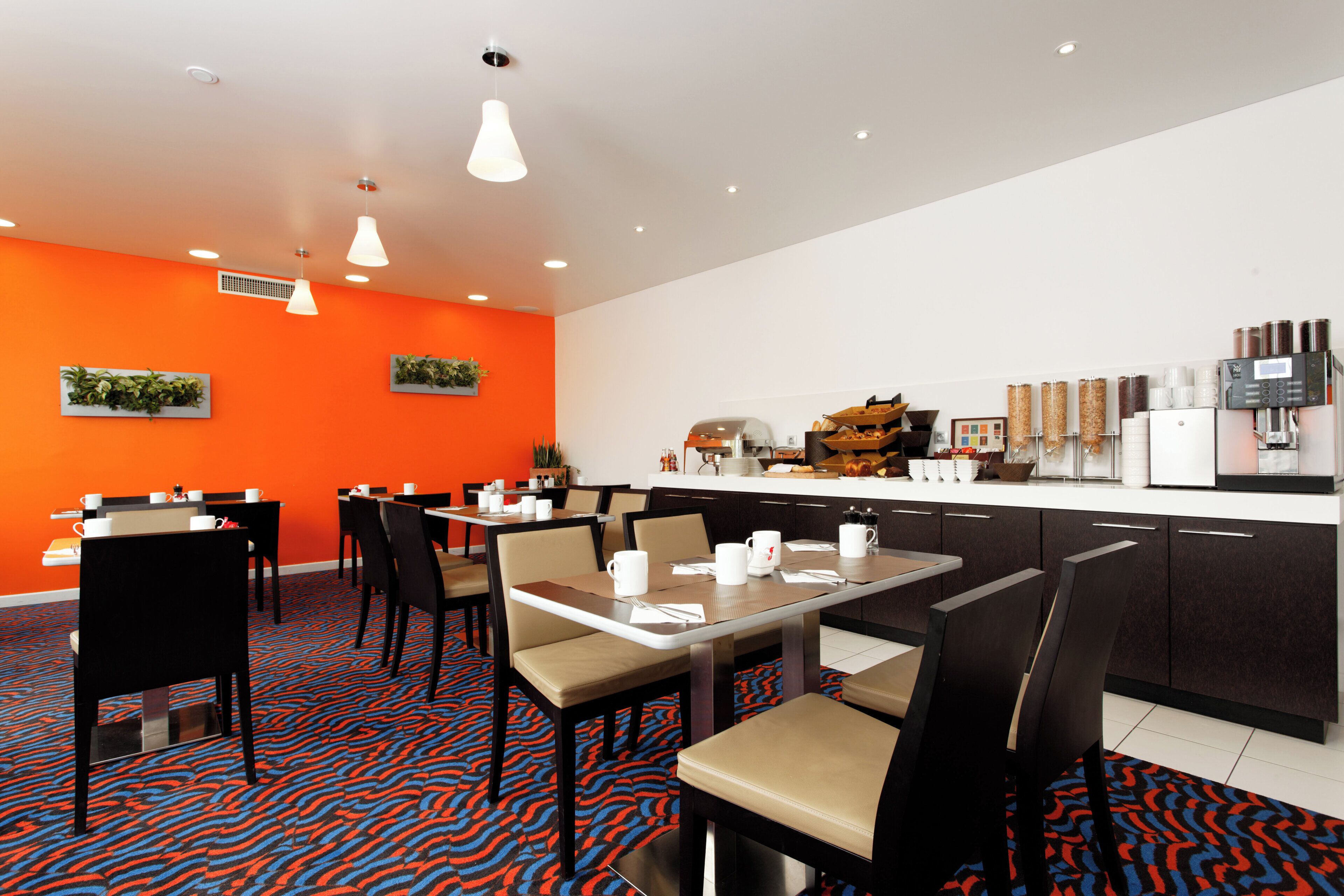 A modern dining area with tables and chairs, a coffee machine, and a kitchen counter with various items.