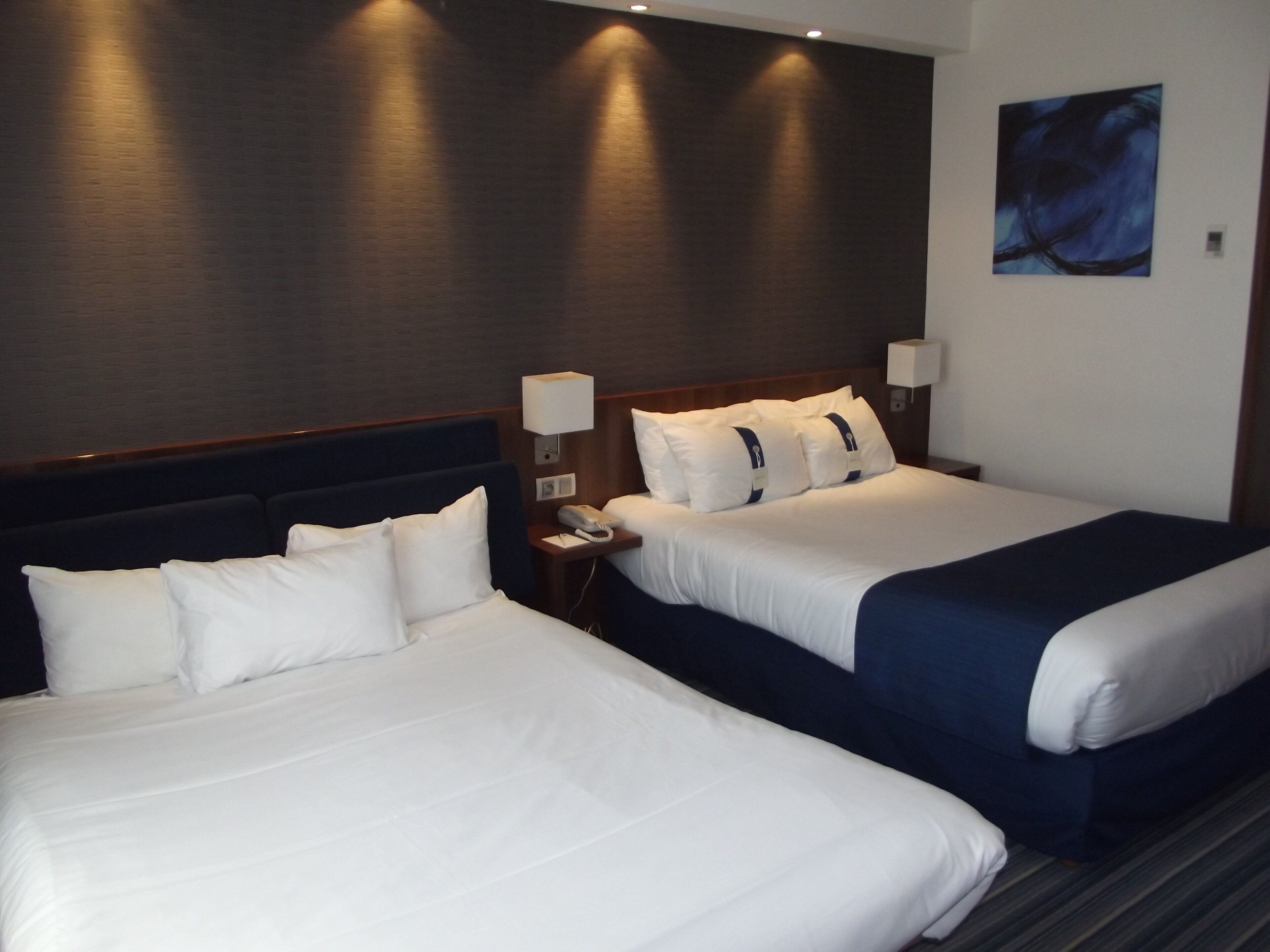 Una habitación de hotel con dos camas, una mesita de noche, una lámpara y un cuadro en la pared.