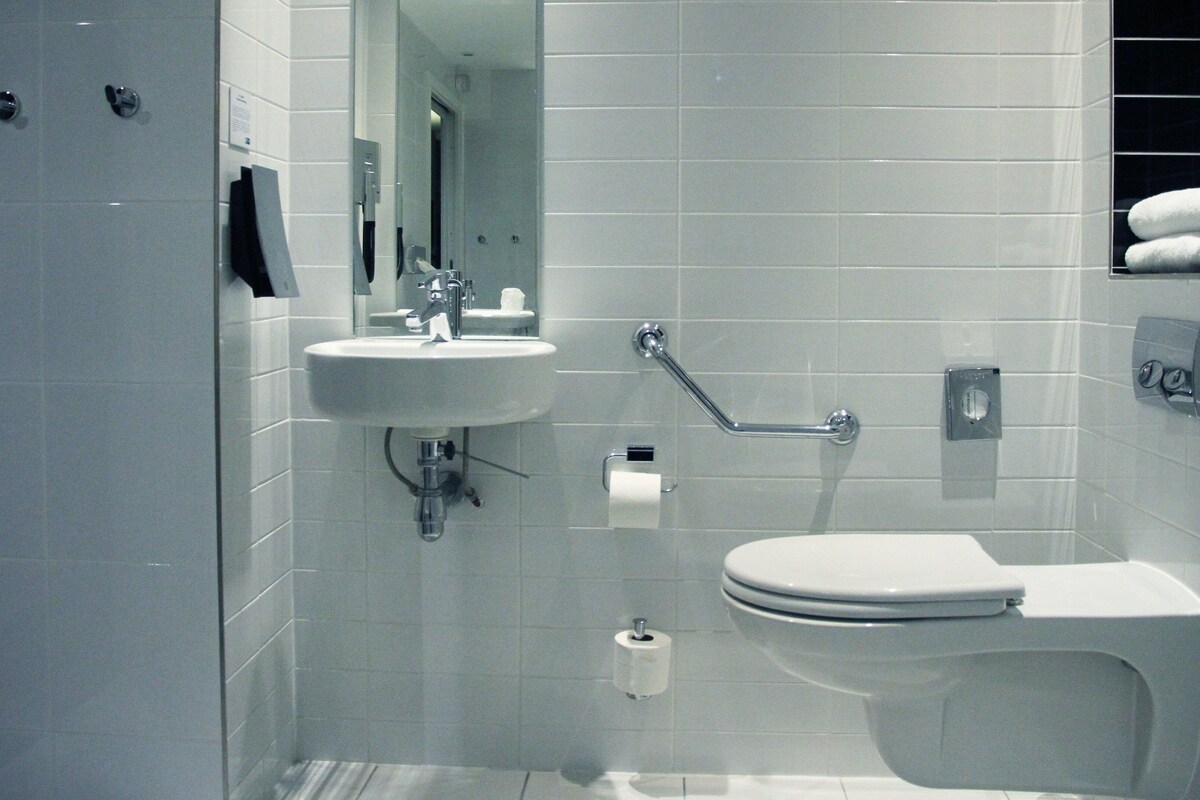 A modern bathroom with a sink, toilet, and handrail.
