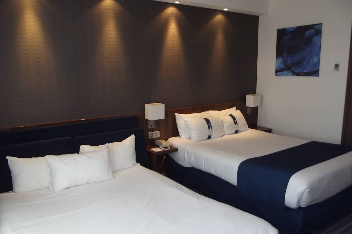 A hotel room with two beds, a nightstand with a lamp, and a painting on the wall.