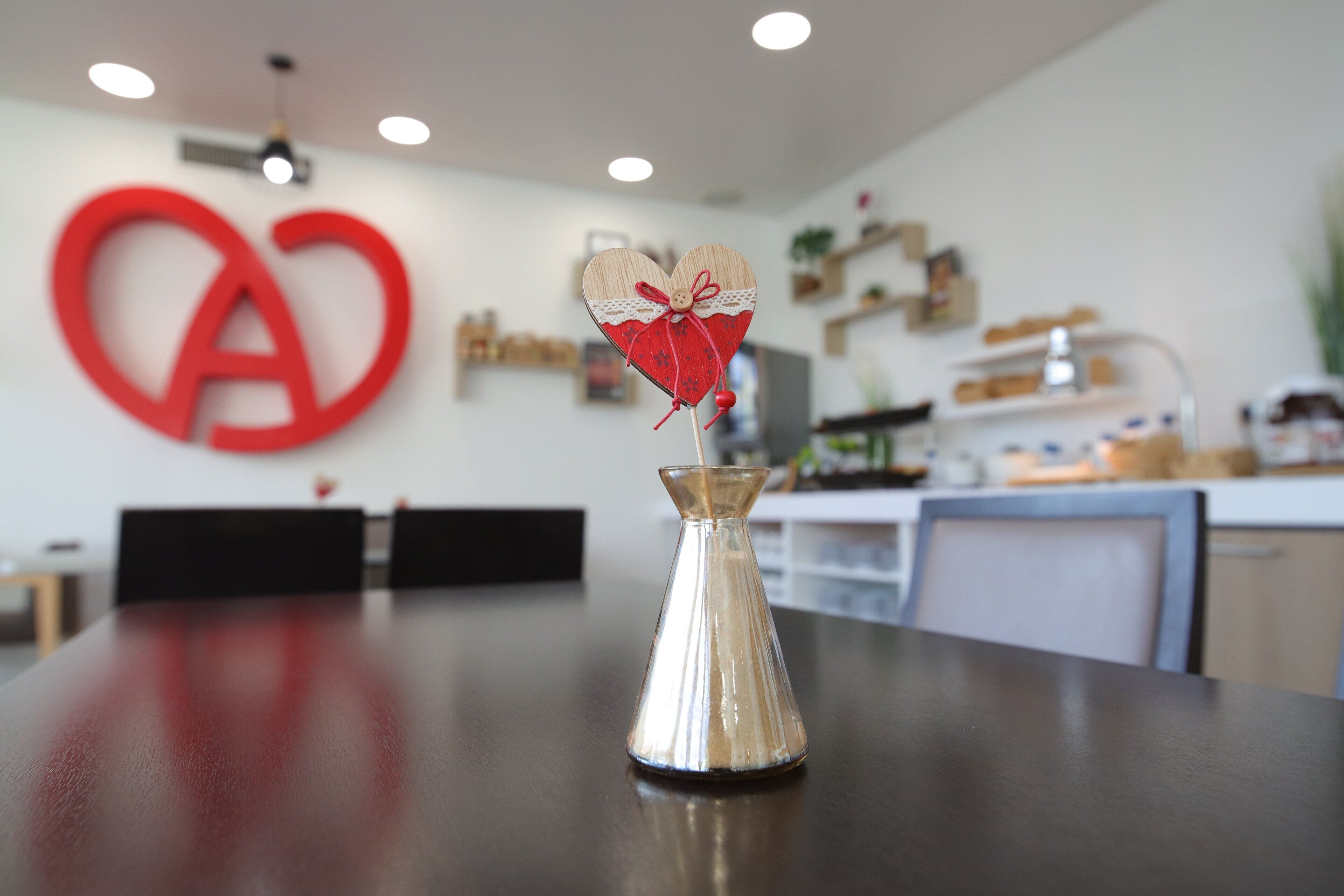 Una cocina con un logotipo rojo grande en la pared, una mesa de madera con un florero, y un diseño moderno.