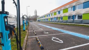 A parking area with electric vehicle charging stations, marked parking spaces, and a building with a modern design.