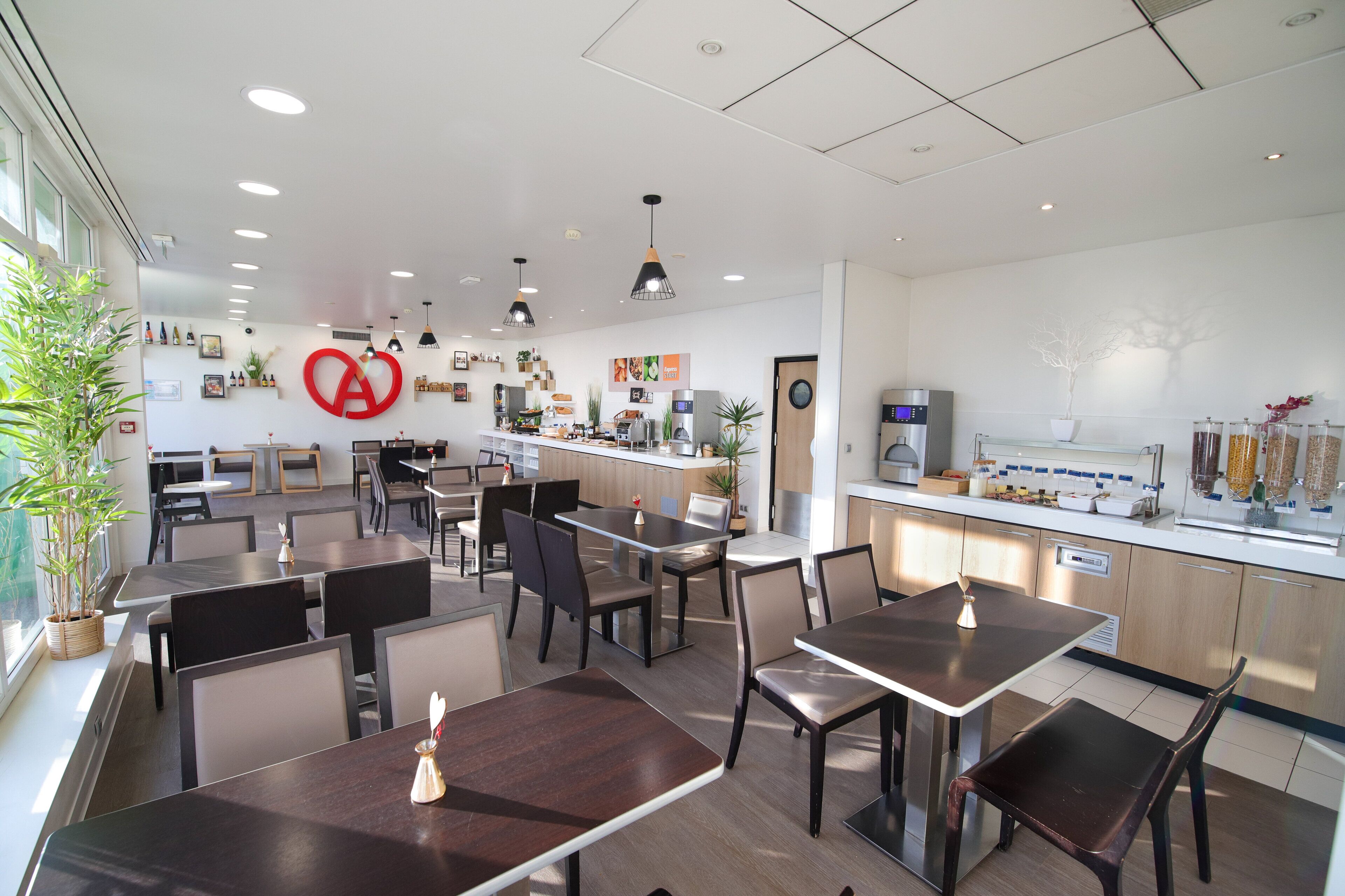 A modern restaurant with a clean, minimalist interior, featuring a central counter, seating area with tables and chairs, and a variety of plants and decorative items on the walls.
