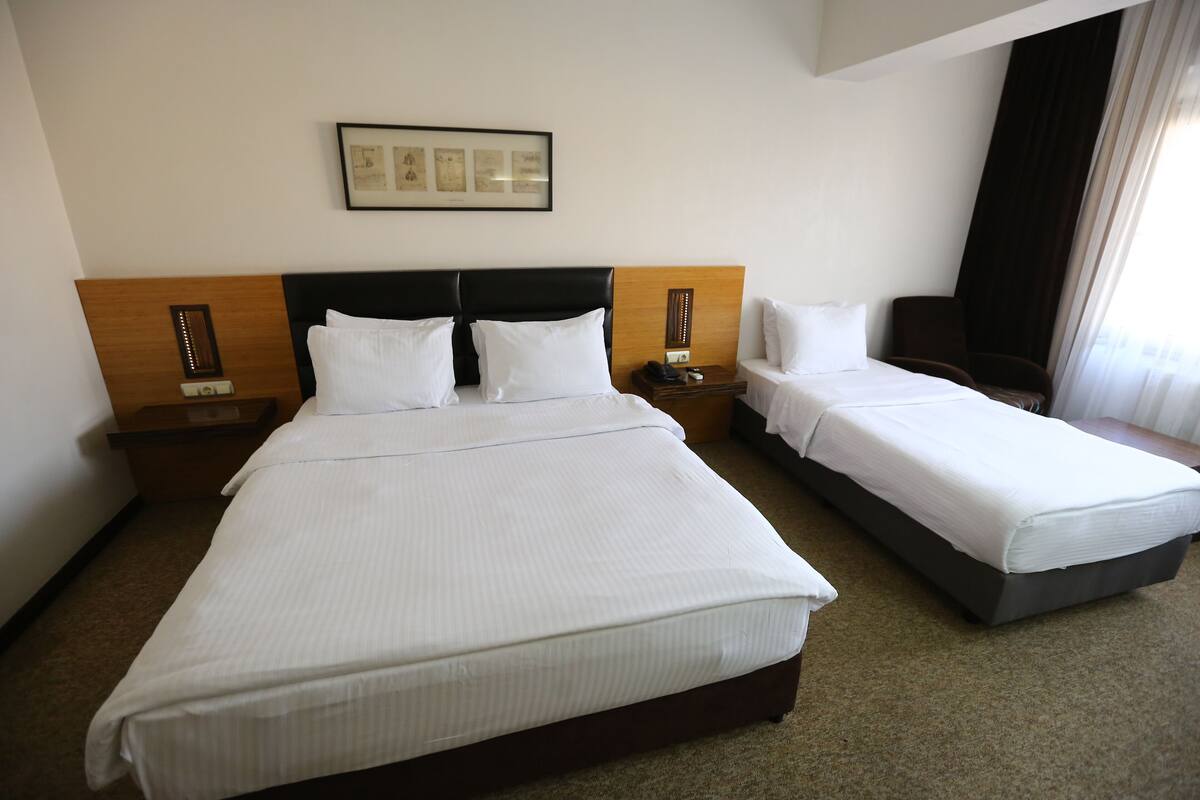 A hotel room with two beds, a headboard, bedside tables, and a framed picture on the wall.