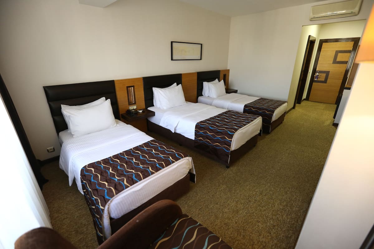 A hotel room with two single beds, a small sofa, and a door leading to another room.