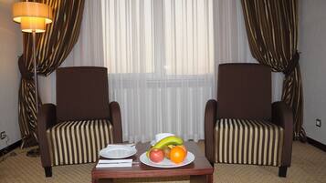 Une chambre d’hôtel avec deux fauteuils marron à rayures, une table en bois sur laquelle est posée une assiette de fruits, et une lampe.