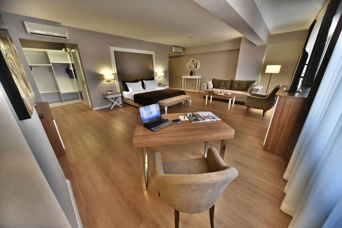 A modern hotel room with a bed, desk, laptop, and seating area.