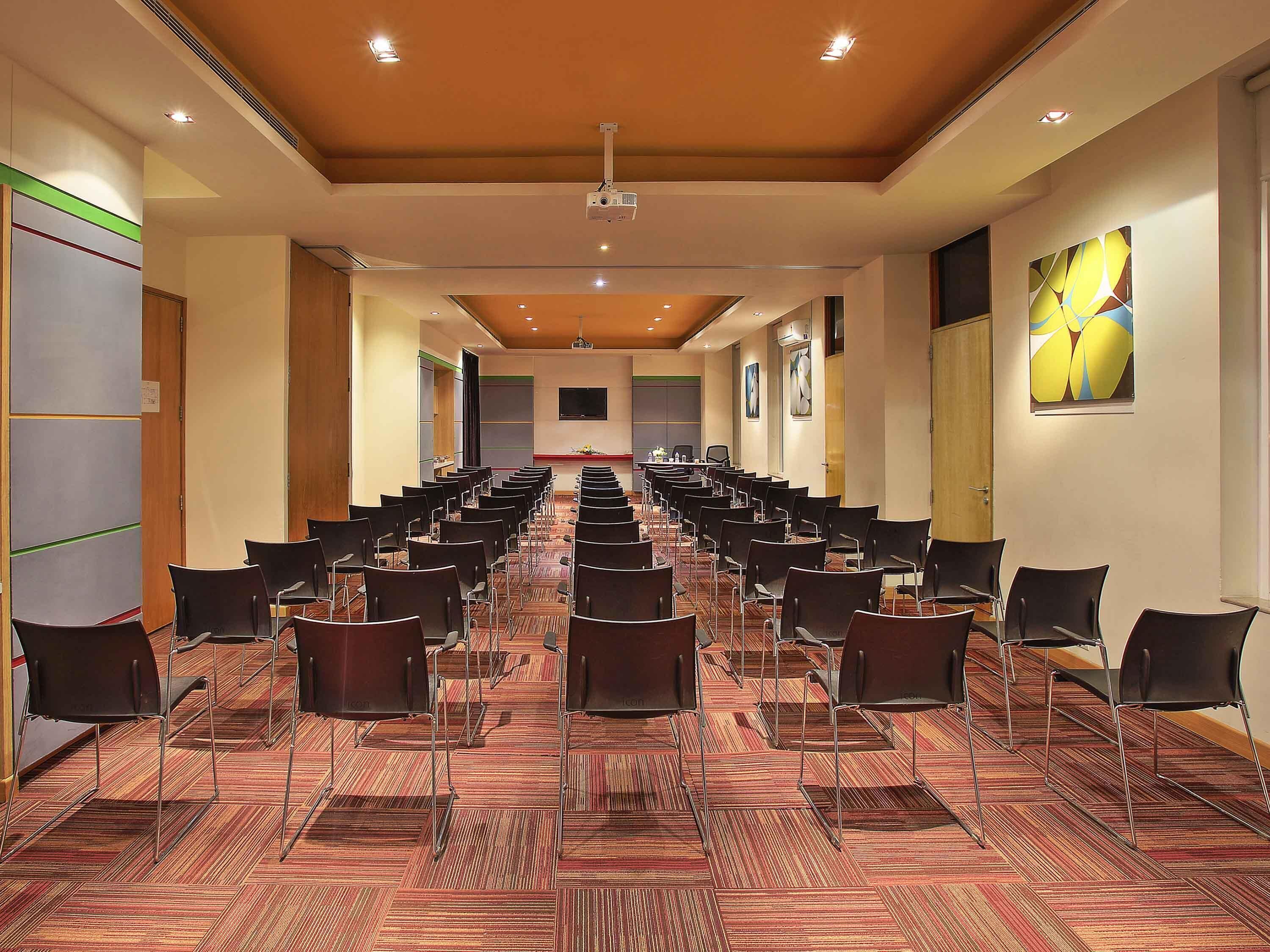 Une salle de conférence avec des rangées de chaises, un projecteur et un grand écran.