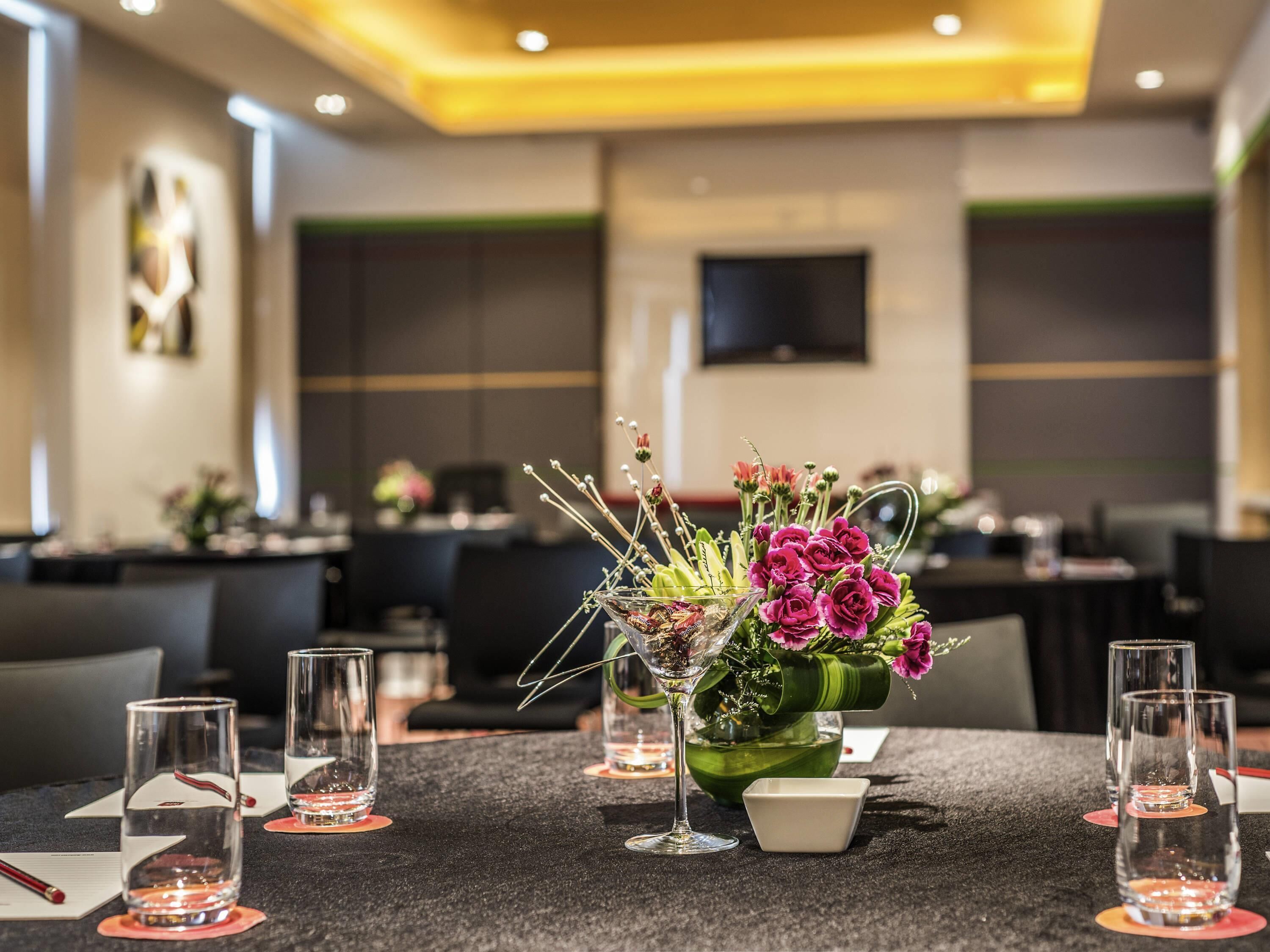 A conference table with a floral centerpiece, clear glasses, and a small white box.