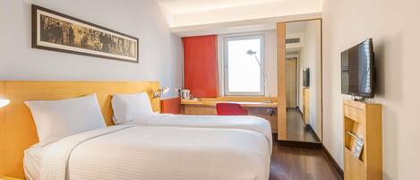 Una habitación de hotel con dos camas, un escritorio, un televisor y una ventana.