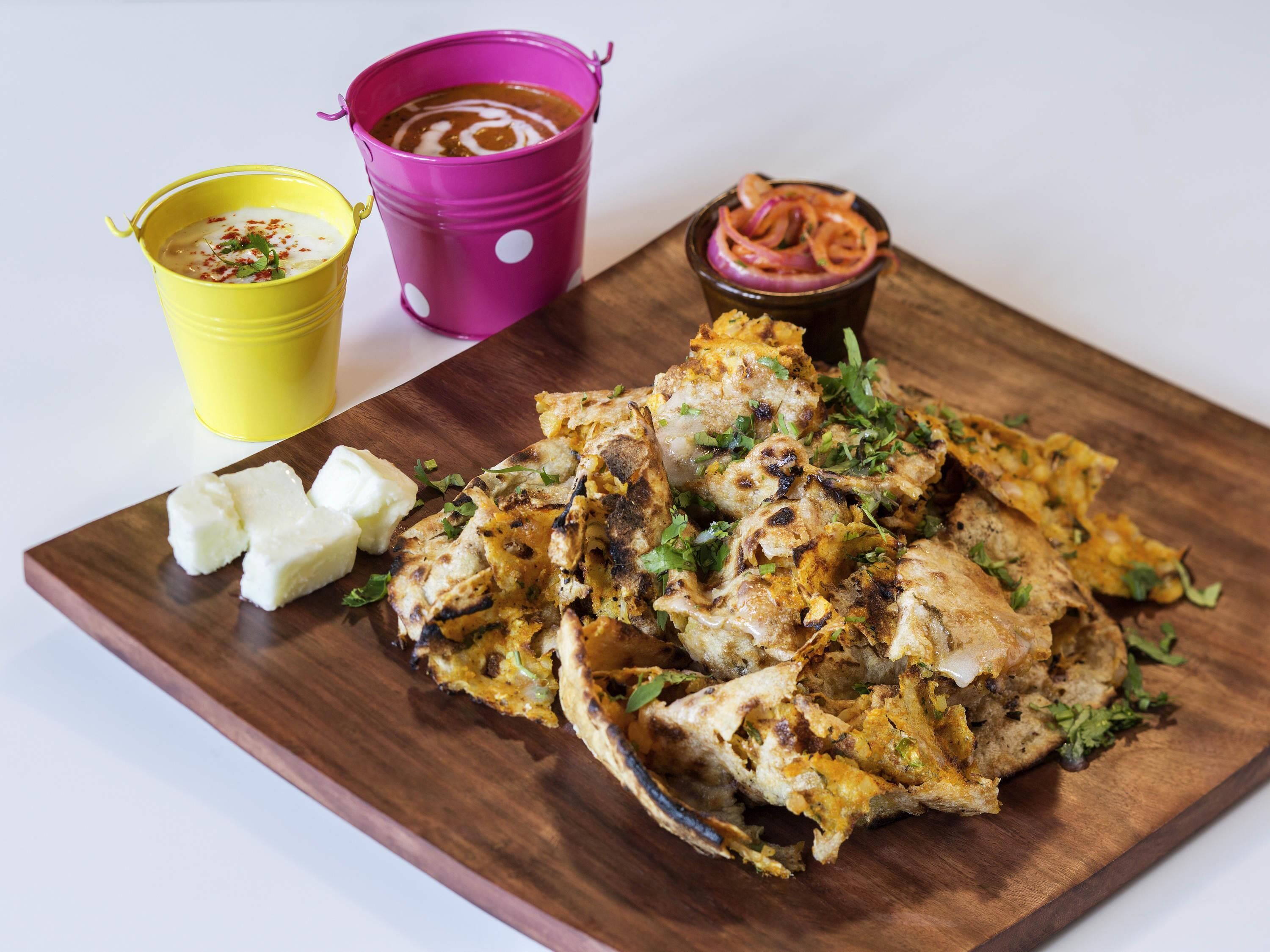 Ein Holzbord mit gegrilltem Hähnchen, einer gelben Tasse und einer violetten Tasse mit Soße.